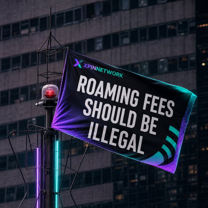 A flag mounted on a pole with a red beacon light displays the message "ROAMING FEES SHOULD BE ILLEGAL" alongside the "XPINNETWORK" logo, set against the backdrop of a dark urban high-rise building.