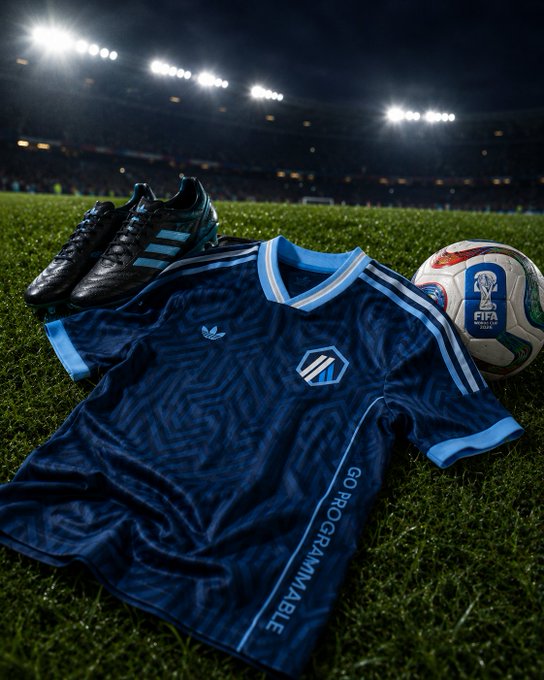 The image features a soccer jersey, shoes, and a soccer ball laid out on a field. The soccer ball is positioned near the center of the image, while the soccer jersey and shoes are spread across the scene. The background shows a stadium filled with lights, indicating that it's nighttime or during an evening game. The text "Go programmable and win" appears in the image, which could be related to a promotional campaign for a sports team or event.