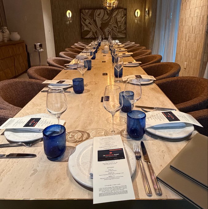 An elegantly set long dining table with white plates, blue glassware, wine glasses, and menus for 'THE WESTERN RESERVE' at each place setting.