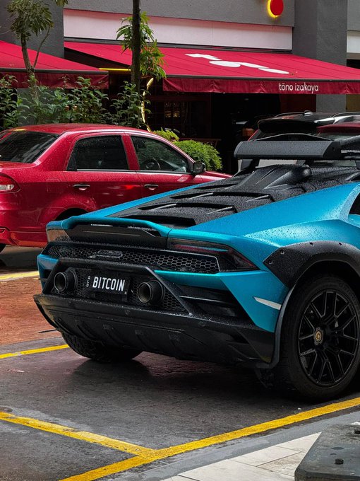 The rear of a blue Lamborghini Huracán Sterrato with a 'BITCOIN' license plate parked in front of a Tono Izakaya restaurant.