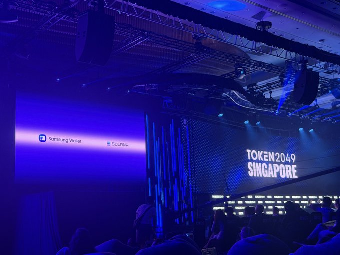 A dimly lit event hall with stage lighting displays 'Samsung Wallet', 'SOLANA', and 'TOKEN2049 SINGAPORE' on large screens.