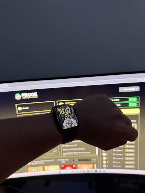 A person displays an Apple Watch with a custom 'FROGE' watch face showing the time 10:02, positioned in front of a computer monitor displaying the FROGE website.