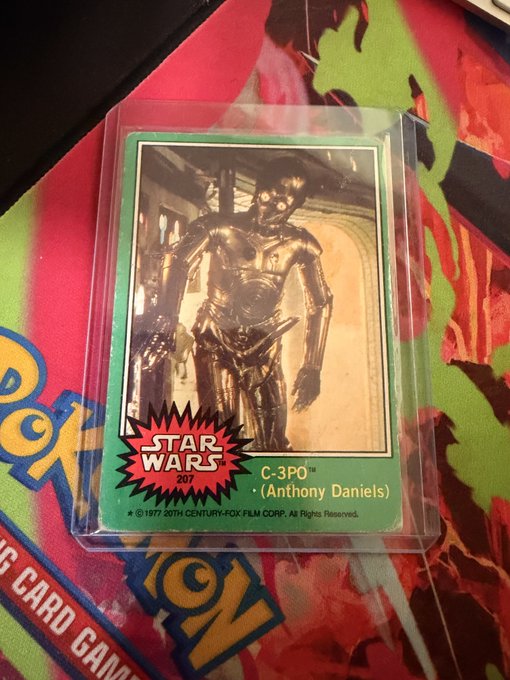 A 1977 Topps Star Wars trading card featuring C-3PO (Anthony Daniels) in card number 207, displayed inside a protective plastic sleeve over a colorful background.