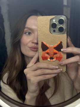 A woman takes a mirror selfie holding a phone with a cork case featuring a geometric orange fox design.