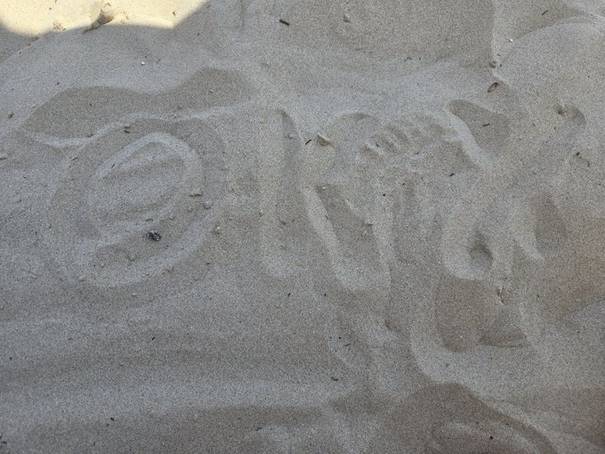 Footprints pressed into light-colored sand on a beach, showing shoe tread impressions.