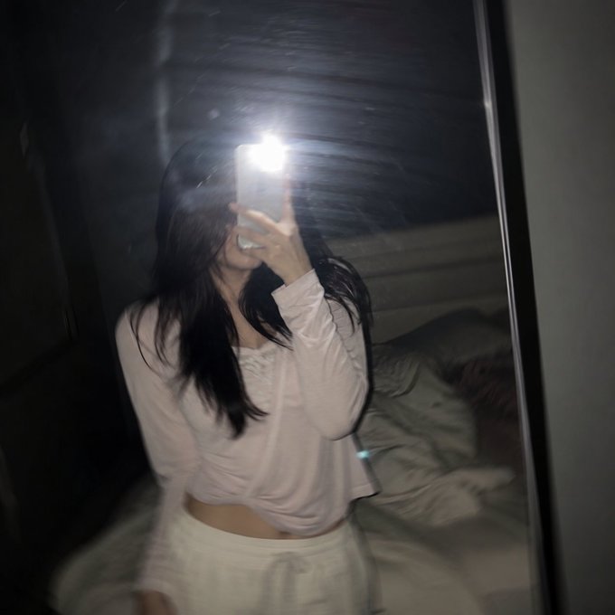 A blurry mirror selfie of a person in a pink long-sleeve crop top and white skirt, with their face obscured by a phone flash. The dark, moody photo complements the "good night" send-off before an NFT hunt with CloudQuest.asia.
