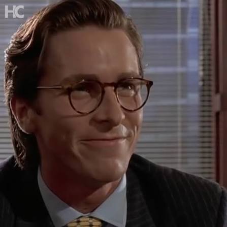 A man wearing tortoiseshell glasses and a pinstripe suit smiles in what appears to be an office setting, with an 'HC' watermark in the corner.