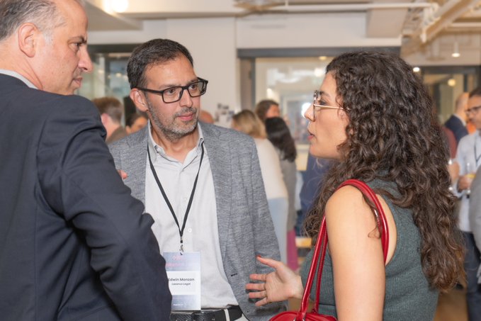 A photograph of three people conversing at what appears to be a networking event, with the central man wearing a lanyard that reads 'Bohan Morstan' and 'Ginance Legal.'
