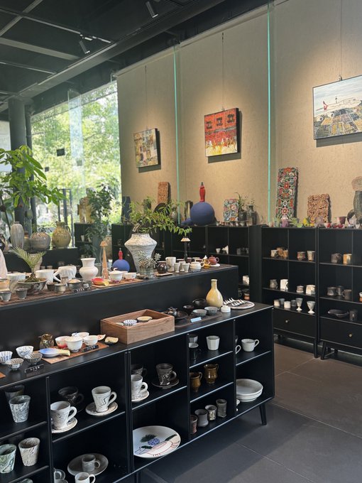 A pottery and ceramics shop displays an array of handcrafted cups, bowls, vases, and decorative pieces arranged on black shelving, with colorful artwork adorning the walls. The serene, treasure-filled space provides a peaceful backdrop that contrasts with the post's discussion of seeking "enlightenment" through relationships and trading, offering a quiet visual metaphor for mindful appreciation over fleeting attraction.