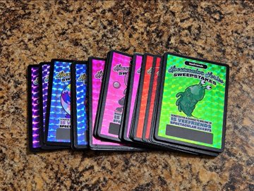A collection of holographic trading cards fanned out on a granite countertop, including a 'Sweetiekins' card with a green creature and various other colorful sports-themed cards with silver and patterned finishes.