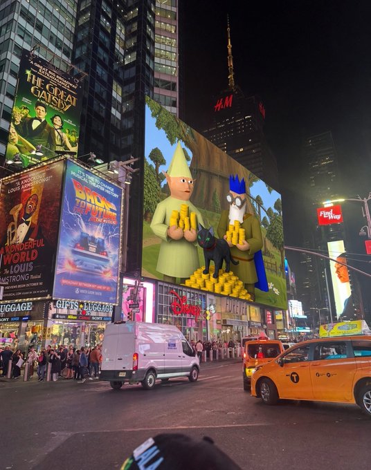 A nighttime view of Times Square in New York City featuring prominent Broadway billboards for "The Great Gatsby" and "Back to the Future: The Musical" alongside a large digital advertisement displaying Simpsons-style characters, with a yellow taxi and a white van on the street.