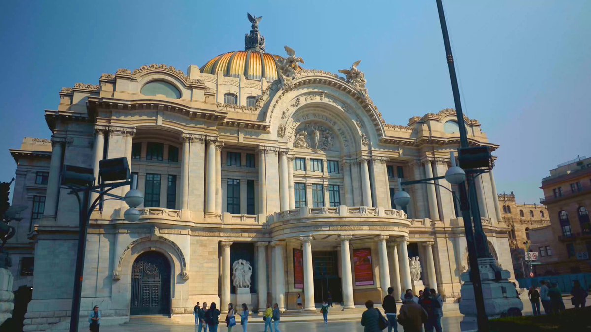 The image shows a large white building with a gold dome, possibly an old architectural structure such as a government or historical monument. The building has many windows and columns, giving it an impressive appearance. A group of people can be seen walking around the base of the building, which is located in Mexico City. Some of them are carrying backpacks, indicating that they might be tourists exploring the area. The image also contains text about Bitcoin, suggesting a connection to the digital currency or possibly a discussion on its impact on the local economy and society.