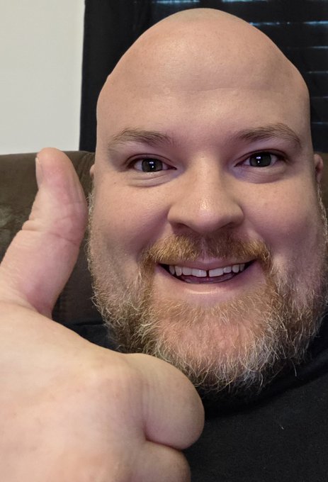 A close-up selfie of a smiling bald man with a red beard giving a thumbs-up gesture.
