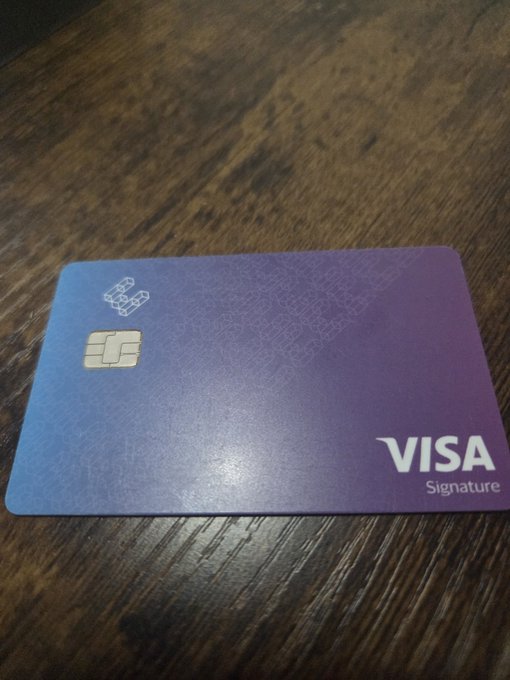 A purple gradient Visa Signature credit card with a chip, resting on a dark wooden surface.