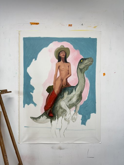 A painting on a canvas in an artist's studio depicts a nude woman wearing a wide-brimmed hat riding a green dinosaur against a pink and blue background.