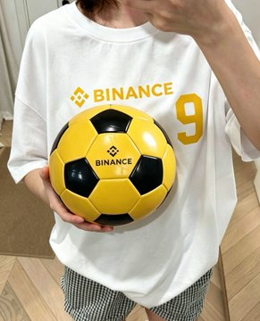 The image features a person wearing a white t-shirt with a yellow soccer ball printed on it. The shirt has the number 9 on the front, indicating that they are a fan of the sport or perhaps have a personal connection to it. The person is standing in a room and appears to be posing for a photo.