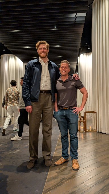 Two men pose smiling for a photo at what appears to be an indoor venue with draped curtains and wooden flooring, with the notably tall man on the left likely being referenced as the Bitcoin developer "Mike" mentioned in the post. The juxtaposition humorously highlights the playful jab that Mike "definitely isn't 'big' bitcoin," given his towering height compared to the shorter man beside him.