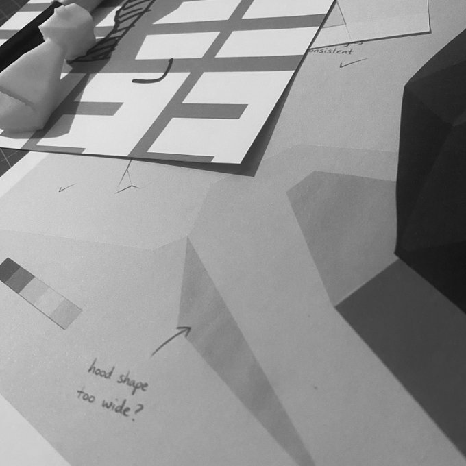 A black and white photo of a designer's workspace with sketches and notes reading 'hood shape too wide?' and 'consistent'.