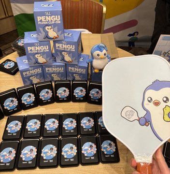 A display of 'PENGU FLIP CLIP-ON' merchandise in blue boxes alongside a large hand mirror featuring the same penguin character design.