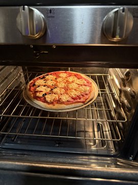 A homemade pepperoni pizza topped with black olives sits on a rack inside an oven.