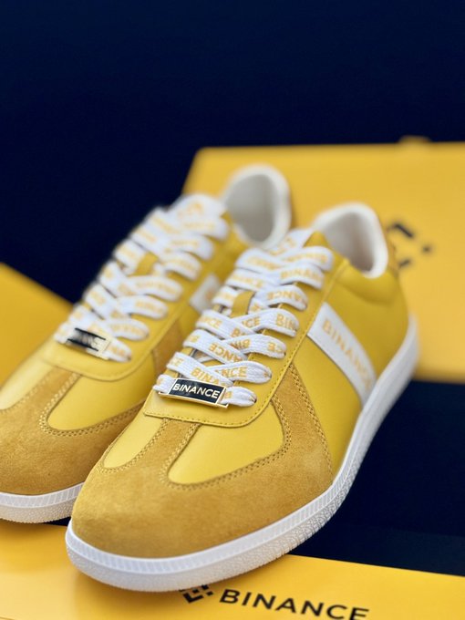 A pair of yellow sneakers with white laces branded 'BINANCE' sit on a yellow Binance-branded box against a dark background.