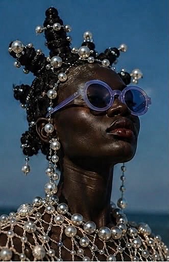 A striking portrait features a dark-skinned model with elaborate pearl-adorned hair, wearing purple round sunglasses and a netted pearl garment against a muted background.