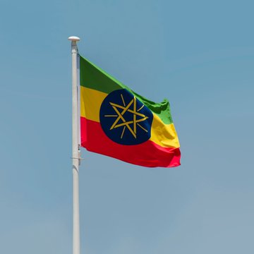 The Ethiopian flag waves against a clear blue sky, symbolizing the nation at the center of a reported decision to cut power to its Bitcoin-mining sector by three-quarters amid strain on its hydroelectric grid.