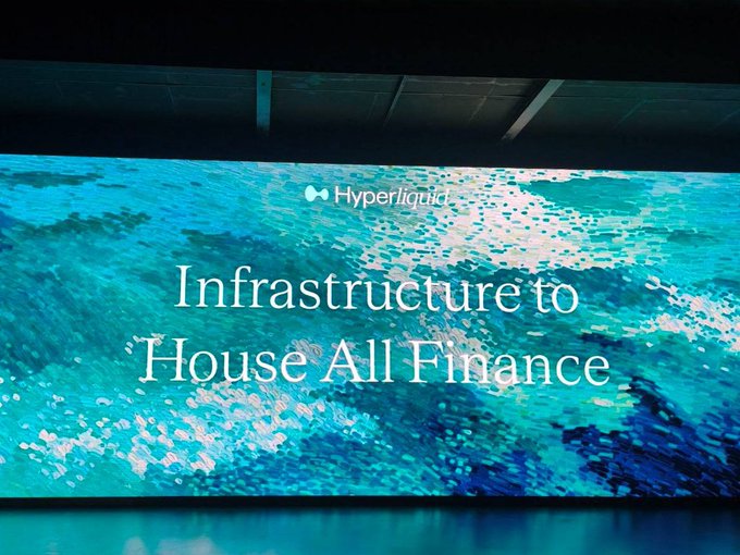 A large digital display showing the text 'Infrastructure to House All Finance' with the 'Hyperliquid' logo, set against a blue, water-like background.