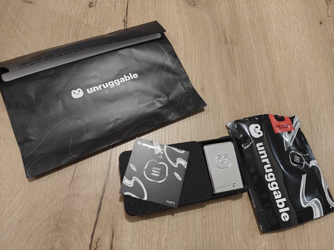 An "unruggable" crypto hardware wallet and its packaging displayed on a wooden surface, with a small card reading "FLIP 3".