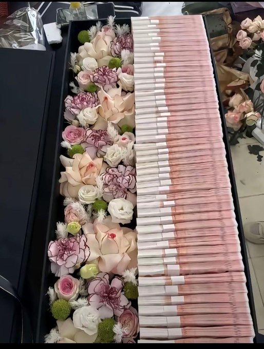 An overhead view of a long black tray filled with an arrangement of pink and white roses, carnations, and other flowers, alongside neatly bundled pink paper straws.