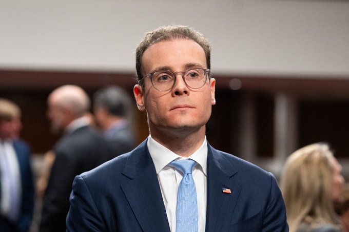 A man in a navy blue suit, light blue tie, and glasses with an American flag pin on his lapel stands in what appears to be a formal setting, possibly a political or business event. The image does not visibly contain any text related to "$ALPHA Arcade" or "$ALGO," so the connection to the post's mention of the Alpha Arcade project on the Algorand blockchain is unclear from the image alone.