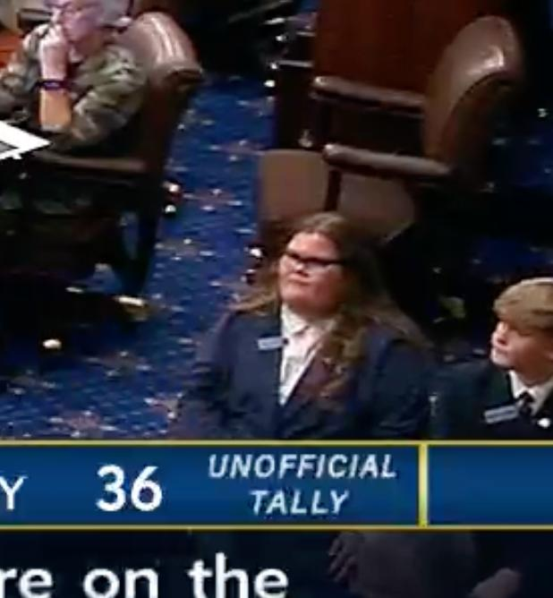 A woman in a suit sits with a satisfied expression in what appears to be a legislative chamber, with an on-screen graphic showing "UNOFFICIAL TALLY 36" as the context playfully suggests she "ate" 36 votes related to the crypto clarity act.