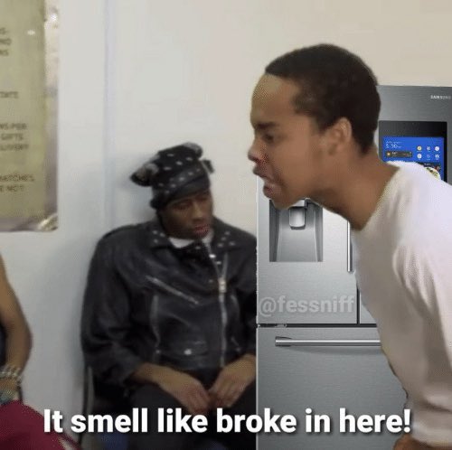 Two men appear in a kitchen next to a Samsung refrigerator, with the standing man saying "It smell like broke in here!" while a seated man in a leather jacket and headwrap looks on. The caption mocks crypto enthusiasts investing in dubious meme tokens during a bear market, with the "smell like broke" punchline suggesting the environment reeks of financial failure.