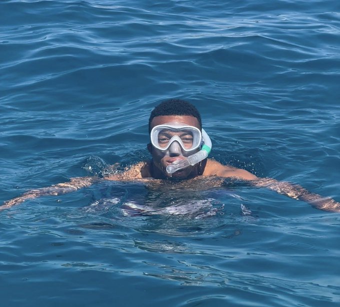 A man wearing a snorkel mask and breathing tube floats in deep blue water with his eyes closed.
