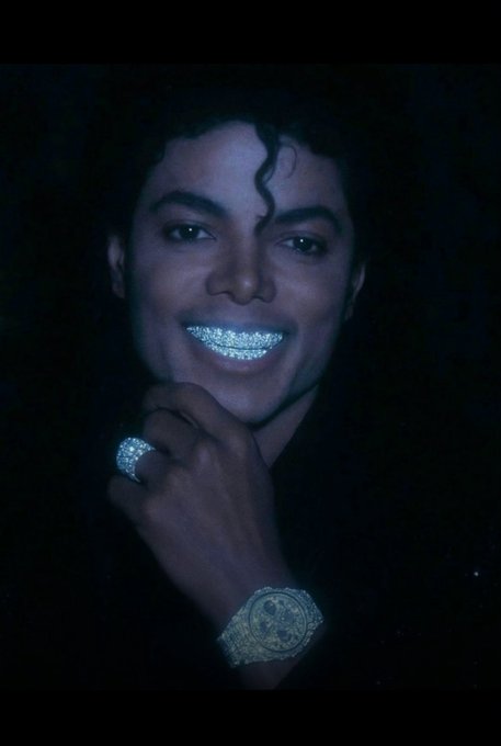 The image shows a smiling man with curly dark hair, wearing a sparkly jeweled grill on his teeth, a large diamond-encrusted ring, and a luxury watch, with his hand resting near his chin against a black background. The caption relates to the post by featuring a recognizable celebrity figure (Michael Jackson) that adds a flashy, high-profile aesthetic to the MetaWin username "Philipmaria1."