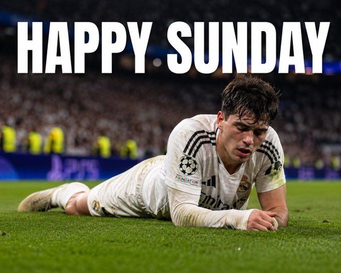 A soccer player in a white Real Madrid kit lies on the grass with 'HAPPY SUNDAY' displayed in large text above him.