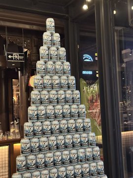 A pyramid display of light blue "Trash Panda" craft beer cans stacked up at what appears to be a bar or restaurant, with an "EXIT" sign visible in the background.