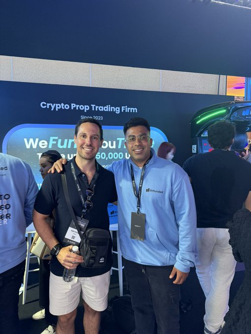 Two men pose together smiling at a crypto conference, with one wearing a "Bitfunded" hoodie, standing in front of a banner for a "Crypto Prop Trading Firm" displaying "WeFundYouUpTo 50,000" since 2023, visually reinforcing the post's mention of meeting Bitfunded friends at the event.
