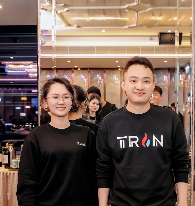 A man and a woman in black sweaters stand together at an event, with the man's sweater featuring the 'TRON' logo.