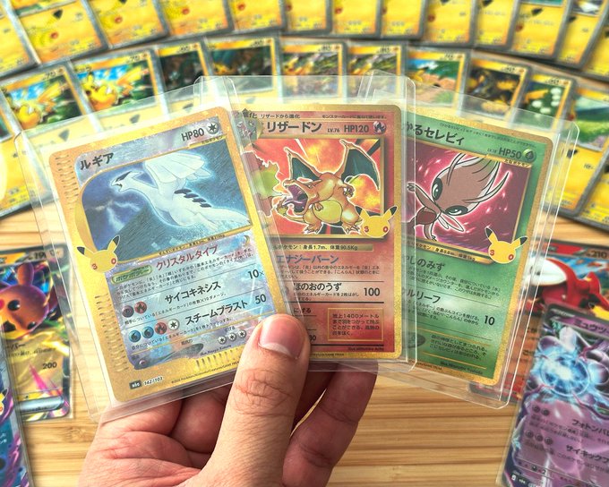 A hand holds three Japanese Pokémon cards in protective sleeves featuring Lugia, Charizard, and Espeon, with more cards displayed in the background.