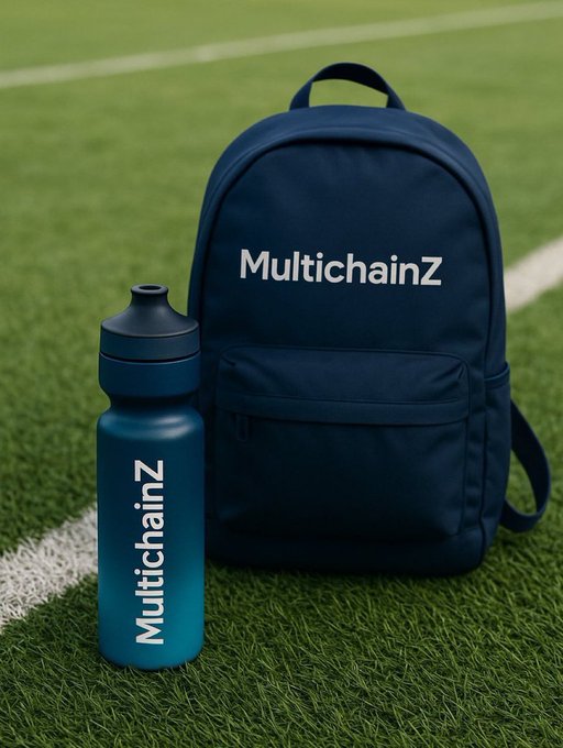 A navy blue backpack branded 'MultichainZ' and matching blue water bottle branded 'MultichainZ' sitting on green artificial turf with a white line.