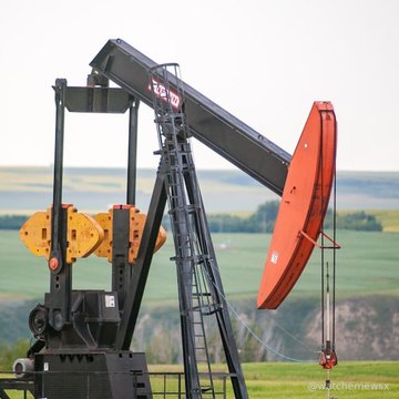 An oil pumpjack with a red and black beam operating in a grassy field with hills in the distance.