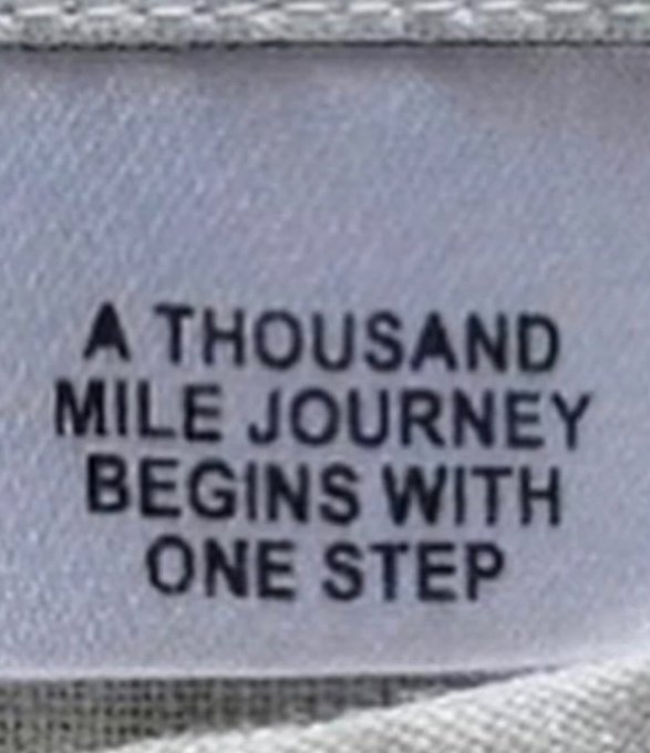 A fabric label or tag with the printed text "A THOUSAND MILE JOURNEY BEGINS WITH ONE STEP."