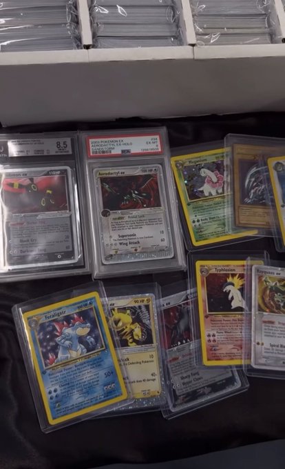 A collection of Pokémon trading cards displayed in protective slabs and cases, including graded cards and a prominent PSA-graded 'Ampharos ex' card.
