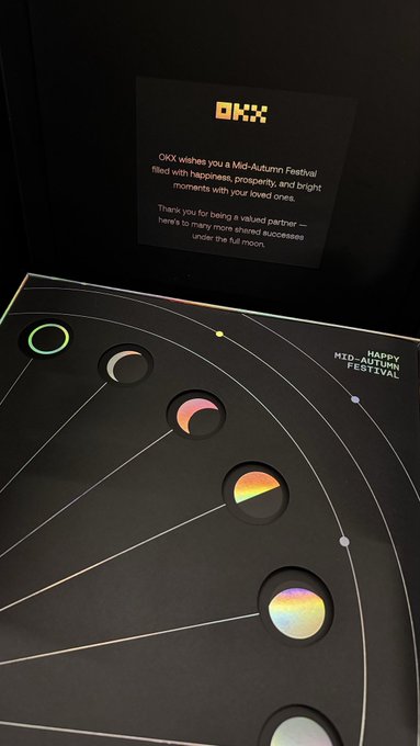 A Mid-Autumn Festival gift set from OKX featuring a card with the message 'OKX wishes you a Mid-Autumn Festival filled with happiness, prosperity, and bright moments' and a display of moon-phase stickers.