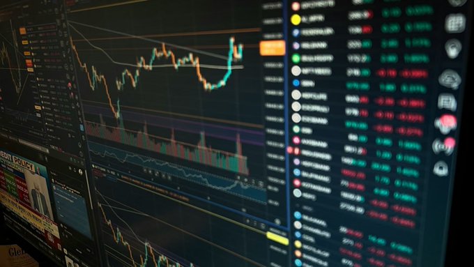 A stock trading screen displays various market data with candlestick charts and rows of ticker symbols, with a visible label reading "IONQ | SPOT" on the lower left, alongside a financial news article about Bitcoin ETF inflows. The image, showing active market data and price movements, visually reinforces the accompanying post's discussion of significant Bitcoin ETF inflows—particularly BlackRock's IBIT—while highlighting that broader ETF trends remain negative for the year.