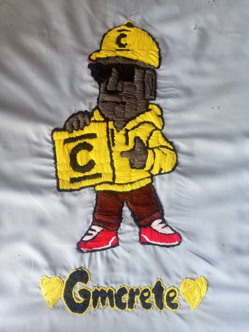 Embroidered on white fabric is a cartoon figure in a yellow cap and hoodie, holding a sign with a "C" logo, paired with the text "Gmcrete" flanked by two yellow hearts—reflecting the creator's custom embroidery for ConcreteXYZ.