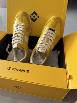 A pair of yellow sneakers displayed inside a yellow Binance-branded shoebox, suggesting a promotional crypto giveaway item.