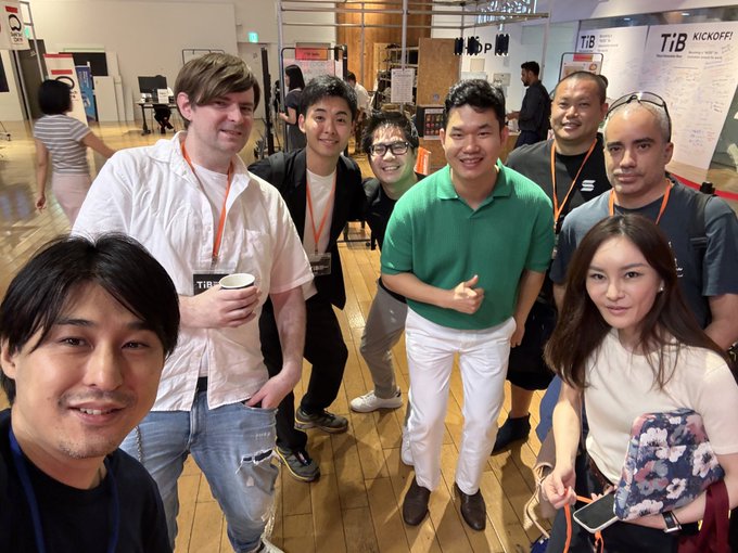 A group of people, including men and a woman, pose for a selfie at what appears to be a startup event, with whiteboards displaying 'TiB KICKOFF' visible in the background.