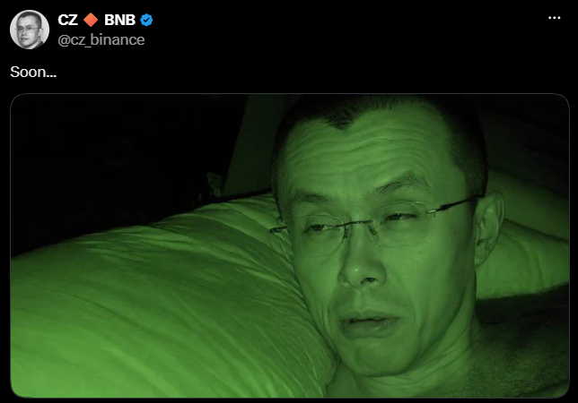 A social media post by CZ (Changpeng Zhao) @cz_binance with the caption 'Soon...', featuring a green-tinted night-vision style photo of him lying down with his head on a pillow.